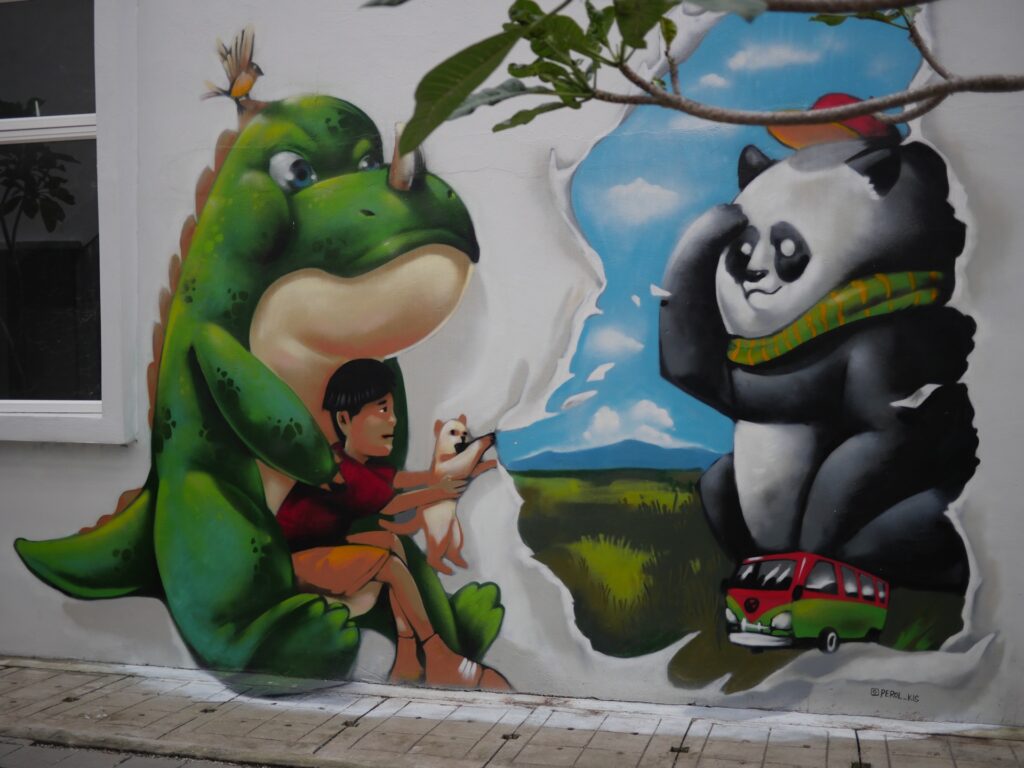 3D Mural of a green dinosaur holding a child with a cat which tears open the wall fabric revealing the traveling panda and a volkswagon hippi van