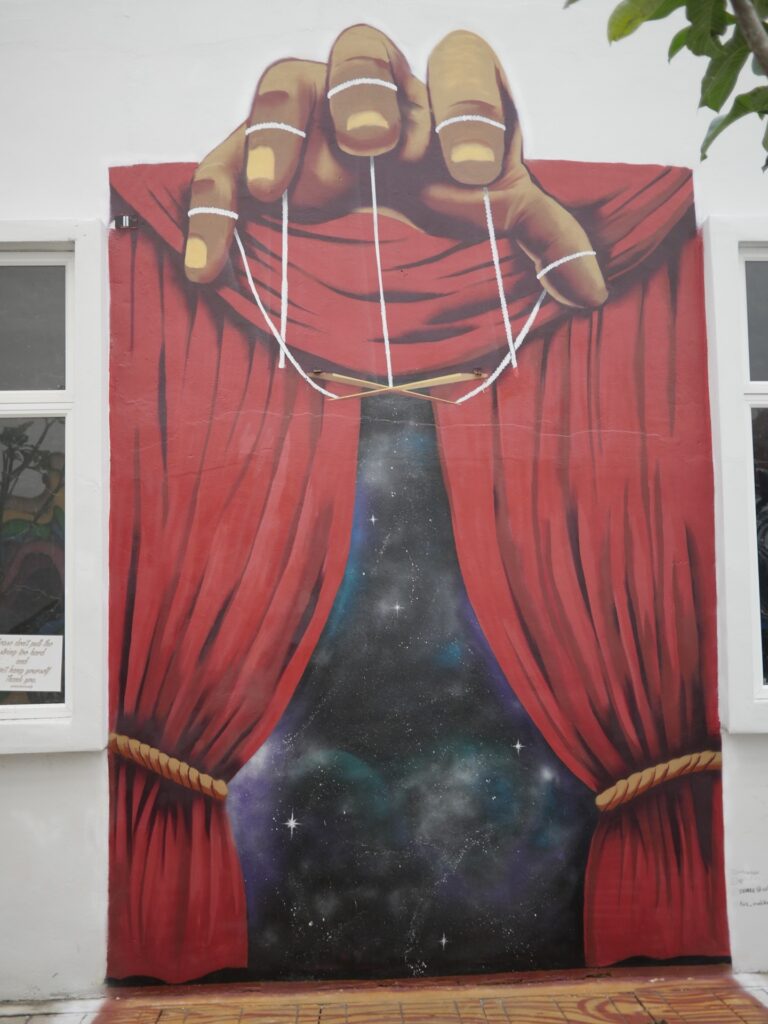 3D Mural showing a huge opening curtain with a huge hand above holding strings and sticks