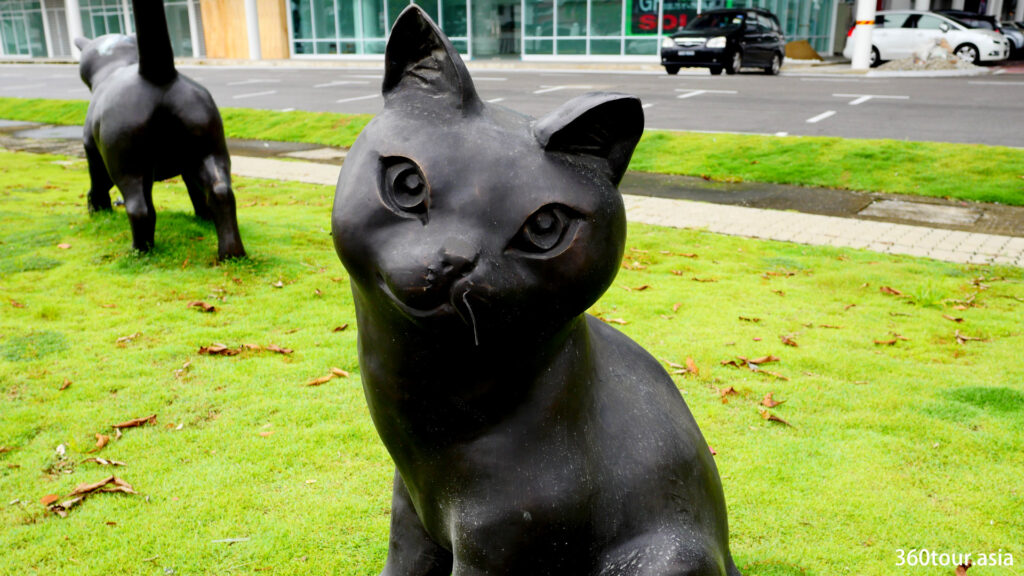 这只青铜猫雕塑描绘了一只可爱的猫，带着微笑看着你