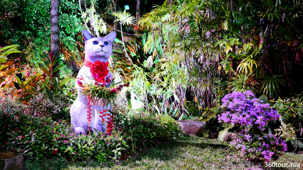 This cat statue is standing lonely within a background of green plants.